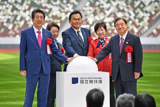 Governor Koike, in a red jacket, stands with Prime Minister Abe